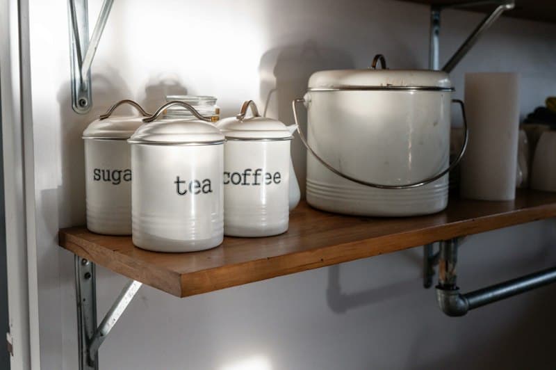 White kitchen canisters labeled sugar, tea, and coffee neatly arranged on a shelf