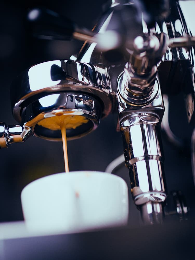 Espresso pouring from a stainless steel portafilter into a ceramic cup