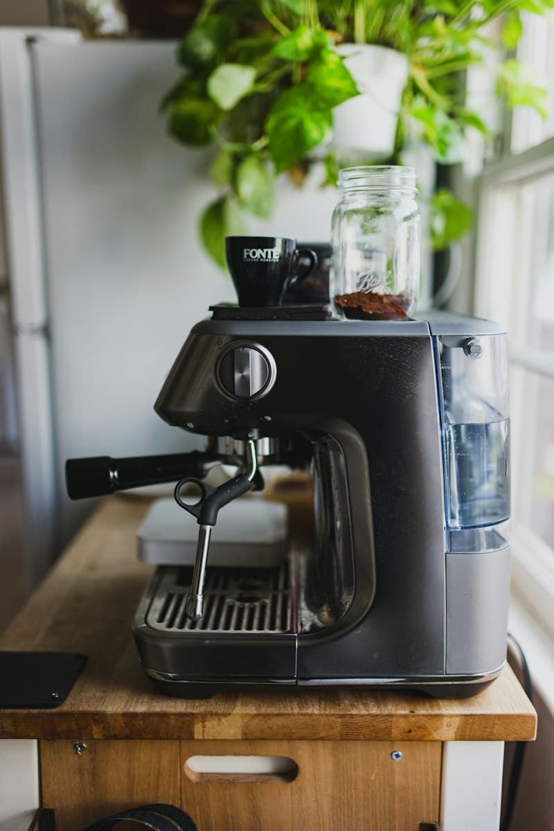 A semi-automatic espresso machine on a butcher block cart by a window, with an espresso cup and a jar of ground coffee on top and a pothos plant behind it